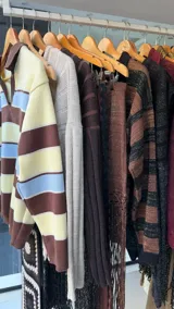 Sweater tejido de punto con diseño a rayas horizontales en tonos amarillo, celeste y marrón. Presenta un cuello polo con escote en V, mangas largas y un corte holgado.