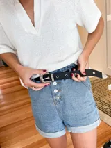 Cinturón negro de cuero con hebilla metálica plateada de estilo western.