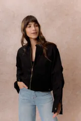 Chaqueta de gamuza sintética color negro, de calce relajado y largo a la cintura. Presenta cuello mao con cierre a presión, cierre frontal metálico, bolsillos delanteros de placa y puños con broche regulable.