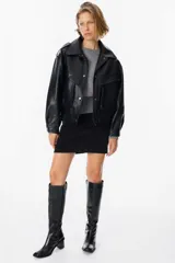 Chaqueta de cuero sintético con textura granulada, corte oversize, cuello camisero, cierre frontal con botones a presión, bolsillos frontales tipo cargo y detalles de charreteras en los hombros.