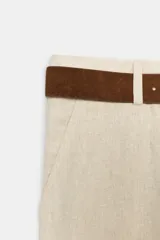 Pantalón culotte de tiro alto color beige, confeccionado con lino. Presenta pernera ancha y corta, bolsillos delanteros y falsos bolsillos de vivo en la espalda. Incluye un cinturón marrón con hebilla metálica redonda y cierre frontal con cremallera, botón interior y gancho.