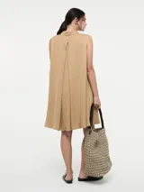 Vestido camisero corto color beige, sin mangas, con cuello clásico, cierre frontal con botones y bolsillos laterales.