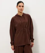 Campera parka de Get Over color marrón, confeccionada en tejido tecnológico de poliéster y elastano. Cuenta con capucha con cordón ajustable, cierre frontal de cremallera, mangas largas con puños elásticos, cintura ajustable con cordón y bolsillos delanteros funcionales. Presenta un diseño amplio con ruedo redondeado.