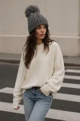 Gorro tejido de punto con diseño de ochos, color gris, con puño acanalado y pompón de pelo sintético en la parte superior.
