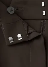Pantalón flare de tiro medio, color marrón oscuro, con aberturas laterales en el bajo, bolsillos laterales y bolsillos de ribete en la parte posterior. Cierre oculto con botón, gancho y cremallera, e incluye forro interior.