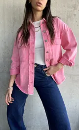 Sobrecamisa rosa de denim con terminaciones desflecadas, cuello camisero, cierre frontal con botones metálicos, dos bolsillos de parche en el pecho y mangas largas con puños abotonados.