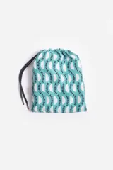 Short de baño celeste con estampado de hojas pequeñas en tonos verdes y blancos. Cuenta con cintura elástica con cordón ajustable, bolsillos laterales y un parche circular con logo en la parte inferior.