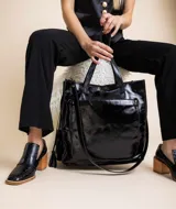 Bolso tipo tote de cuero charolado color negro, con doble asa corta y correa larga extraíble. Tiene bolsillo exterior con cierre y llavero colgante.