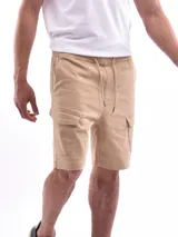 Bermuda cargo color beige, con cintura elástica y cordón ajustable. Presenta bolsillos laterales y bolsillos cargo con solapa en los costados.