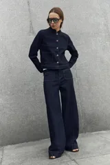 Pantalón de jean azul oscuro con corte flare, tiro alto y bolsillos delanteros tipo plaqué. Presenta costuras a la vista y una silueta amplia en las piernas.