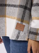 Sobrecamisa de corte holgado con estampado de cuadros en tonos gris, blanco y mostaza. Presenta cuello clásico, cierre frontal con botones, mangas largas con puños abotonados y bolsillos frontales con solapa.