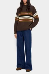 Sweater de punto de corte holgado, con cuello redondo y mangas largas. Presenta un diseño de rayas horizontales en tonos tierra, crema, negro y un detalle en rosa, sobre una base de color marrón.