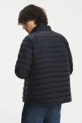 Campera puffer de color negro con cuello alto y cierre frontal completo. Presenta un diseño acolchado con costuras horizontales y bolsillos laterales con cierre.