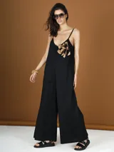 Mono largo negro de bretel fino con escote en V y detalle de flor en el pecho.