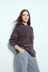 Buzo canguro de calce relajado, color marrón con efecto lavado y costuras a la vista en contraste. Cuenta con capucha integrada y bolsillo frontal tipo canguro.