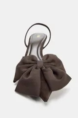 Zapato destalonado de tacón medio con punta fina, acabado en color marrón y detalle de lazo decorativo en la parte delantera. Cuenta con una tira elástica trasera para mayor sujeción.