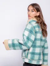 Tapado corto con diseño a cuadros en tonos violeta, rosa y blanco. Cuenta con interior de corderito color beige y cierre frontal con cremallera diagonal.