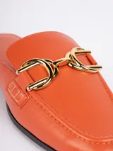 Zuecos abiertos de símil cuero color negro, con punta cuadrada, aplique metálico dorado en la parte superior y taco bajo.