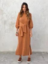 Vestido largo color verde militar, con cuello redondo, mangas largas abullonadas con puños elásticos y detalle de lazo anudado en la cintura. Presenta una abertura lateral en la falda.