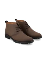 Bota corta de cuero marrón, estilo chukka o desert boot, con cordones y suela de goma negra gruesa y dentada.