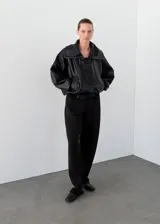Parka oversize de cuero de piel de ovino color negro, con cuello embudo, solapas amplias y cierre oculto de cremallera y botones. Cuenta con manga larga con puños elásticos y dos bolsillos laterales.
