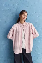 Camisa de calce relajado a rayas rosadas y blancas, con cuello camisero clásico y frente abotonado. Presenta recortes con cambio de dirección en las rayas y silueta amplia.