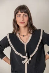 Cárdigan negro de punto fino con hilos de lurex, cuello en V calado con volados color crema, cierre frontal con botones con strass y puños anchos con ribete color crema.