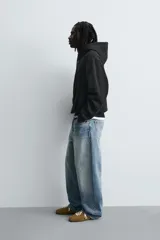 Sudadera tipo hoodie de corte relajado, confeccionada en tejido de algodón con interior cepillado. Presenta capucha con cordones ajustables, bolsillo frontal tipo canguro y terminaciones en rib en puños y ruedo.