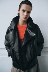 Chaqueta de estilo biker confeccionada en tejido efecto piel con acabado brillante. Presenta cuello con solapas, cierre frontal con cremallera y botones, bolsillos delanteros y bajo ajustable con trabillas y hebilla metálica.