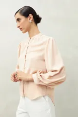 Camisa color marrón claro con cuello mao, mangas 3/4 abullonadas y cierre frontal con botones. Presenta pequeños pliegues en los hombros y detalle calado sutil.