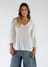Blusa de algodón color gris oscuro con efecto gastado, mangas largas amplias con múltiples volados escalonados y terminaciones deshilachadas.