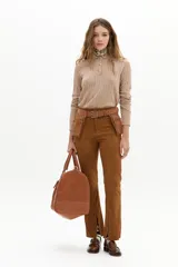 Pantalón de corte recto confeccionado en gamuza de cabra color marrón tostado. Presenta tiro medio con elástico interno en la cintura, cierre frontal con gancho metálico y tajos en el ruedo.