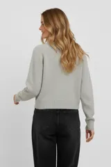 Cardigan de punto color beige, de corte holgado y diseño corto. Presenta cuello redondo, cierre frontal con botones de distintos colores y mangas largas con puños acanalados.