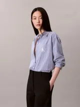Camisa Calvin Klein de corte regular, con diseño de rayas verticales en tonos azul y blanco. Cuenta con cuello camisero, cierre frontal de botones, mangas largas y un bolsillo aplicado en el pecho con el logo bordado de la marca.