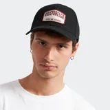 Gorra de béisbol negra con parche frontal bordado en tonos blanco y bordó con la inscripción Kristobelga Goods vs Services.