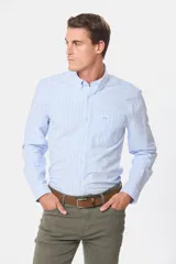 Camisa de corte clásico confeccionada en tela oxford de algodón, con diseño de rayas verticales finas en color celeste y blanco. Presenta cuello abotonado, cierre frontal con botones y bolsillo en el pecho.
