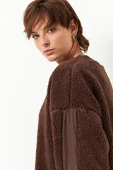 Buzo negro de tela tipo teddy, de manga larga y cuello redondo. Presenta recortes de nylon en mangas y laterales.