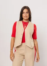 Chaleco beige con escote en V, sin mangas y cierre frontal con botones. Presenta pespuntes en color rojo y logo bordado en la espalda.