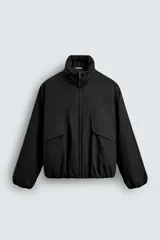 Cazadora acolchada de corte boxy fit, color negro, con cuello subido, cierre frontal de cremallera, bolsillos con solapa en la cadera y bajo con acabado elástico.