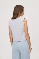 Remera sin mangas negra con cuello redondo y hombros estructurados con hombreras, de corte recto y largo a la cintura.