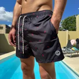 Short de baño negro con estampado de siluetas rojas, cintura elástica con cordón blanco y logo de la marca en la pierna.