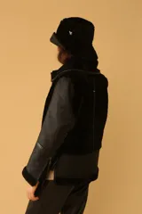 Campera tipo gamulán de cuero negro con interior y detalles en piel sintética negra, cierre frontal y cuello con hebillas ajustables.