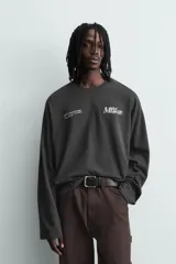 Camiseta de manga larga y cuello redondo con corte relajado, color gris oscuro, con estampado de texto en contraste en el pecho.