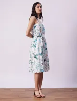 Vestido midi blanco con estampado floral celeste y verde, escote recto con tirantes, abertura frontal con botones, lazo en la cintura y bolsillos laterales.