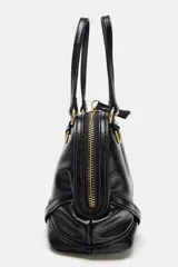 Bolso mini de mano color negro con acabado brillante, diseño estructurado y herrajes dorados. Cuenta con asas de mano fijas y cierre superior mediante cremallera.