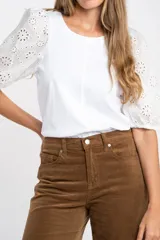 Remera de algodón color rosado con mangas cortas abullonadas de broderie con diseño floral calado. Presenta cuello redondo y costura vertical central en el frente.