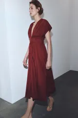 Vestido midi de color bordó con escote en pico y mangas cortas. Presenta un diseño con pinzas, cierre frontal con botones ocultos y un cinturón fino tipo cordón en el mismo tejido para ajustar a la cintura.