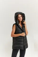 Chaleco negro oversize con capucha forrada en tela gamuzada, cierre metálico YKK, bolsillos laterales y tancas regulables en el ruedo.
