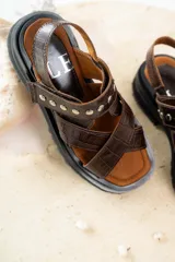 Sandalias de cuero marrón con textura de cocodrilo, diseño de tiras cruzadas con tachas metálicas plateadas y suela track negra de plataforma.