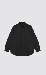 Chaqueta tipo overshirt de microfibra, color negro, con calce oversize y ruedo curvo. Presenta cierre frontal con broches a presión, bolsillos frontales de gran tamaño y cierres laterales a lo largo de las mangas para ajustar su amplitud.